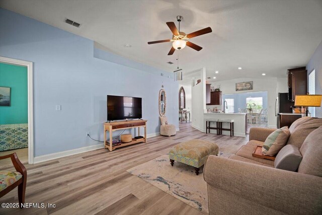 living area with ceiling fan, visible vents, light wood-style flooring, baseboards, and vaulted ceiling
