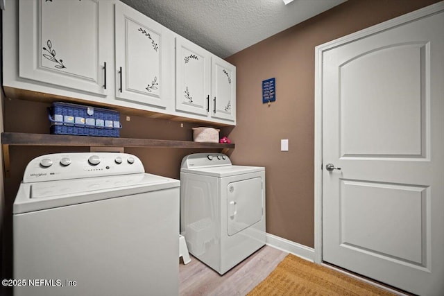 laundry room featuring cabinet space, a textured ceiling, light wood-style flooring, baseboards, and washer and clothes dryer