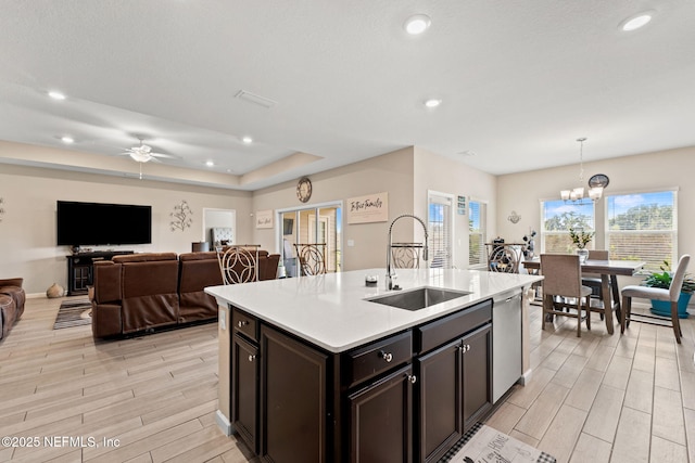 kitchen with a sink, light countertops, ceiling fan with notable chandelier, and light wood finished floors