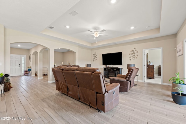 living area with visible vents, a ceiling fan, light wood-type flooring, a raised ceiling, and arched walkways