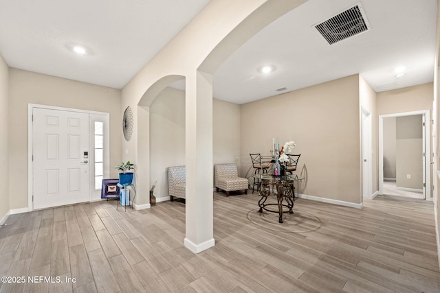entrance foyer with visible vents, arched walkways, light wood-style floors, and baseboards