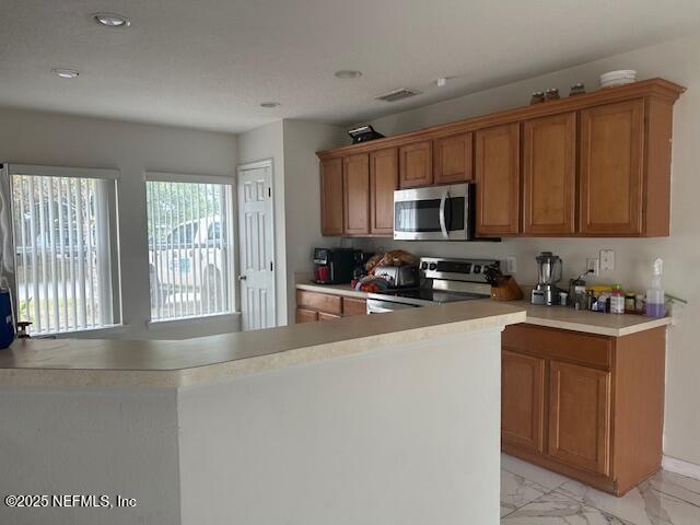 kitchen with brown cabinetry, marble finish floor, light countertops, and appliances with stainless steel finishes