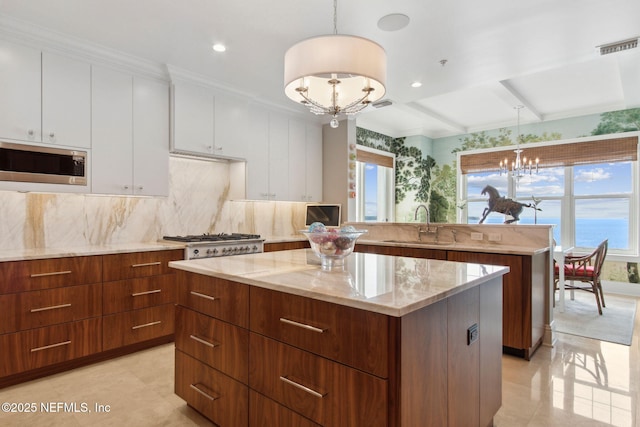 kitchen with a chandelier, stainless steel microwave, a center island, a sink, and white cabinets