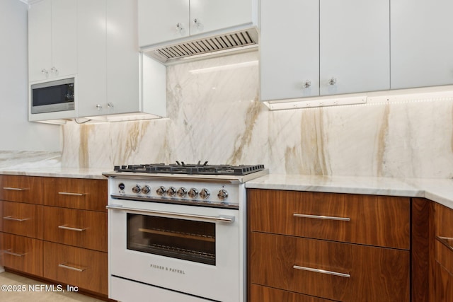 kitchen featuring high end range, exhaust hood, stainless steel microwave, and light stone countertops