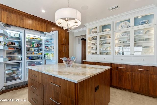 kitchen with a kitchen island, ornamental molding, light stone countertops, a chandelier, and hanging light fixtures
