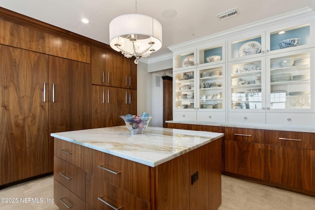 kitchen featuring a center island, light stone countertops, a chandelier, pendant lighting, and glass insert cabinets