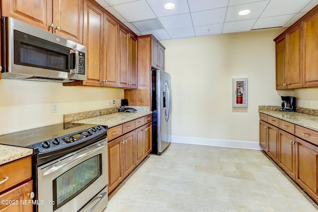 kitchen with stainless steel appliances, baseboards, brown cabinets, light stone countertops, and recessed lighting