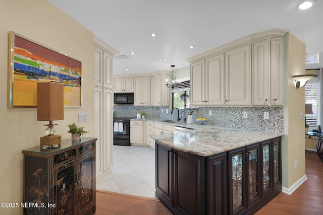 kitchen featuring black appliances, a sink, a chandelier, backsplash, and light stone countertops
