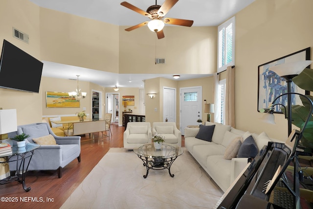 living room featuring a chandelier, a ceiling fan, healthy amount of natural light, wood finished floors, and a high ceiling