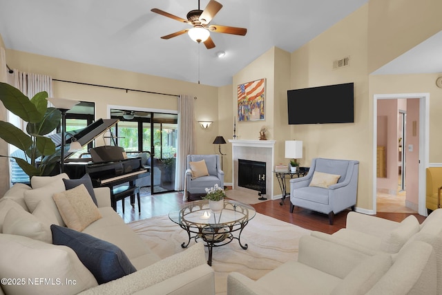 living area featuring ceiling fan, wood finished floors, high vaulted ceiling, a fireplace with flush hearth, and baseboards