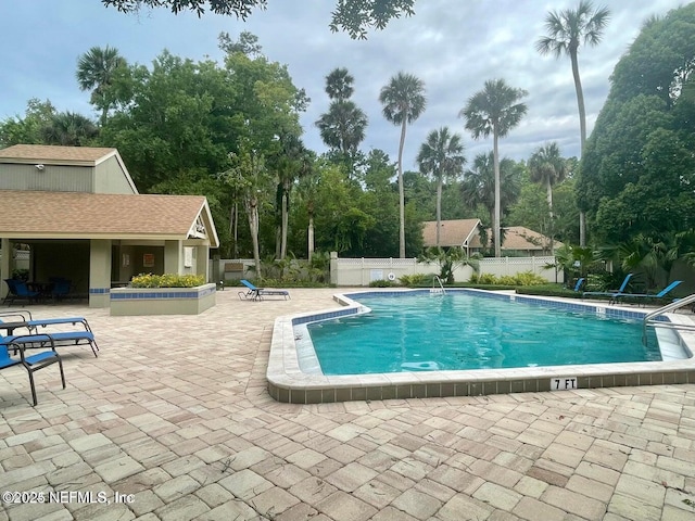 community pool featuring a patio, fence, view of wooded area, and an outbuilding