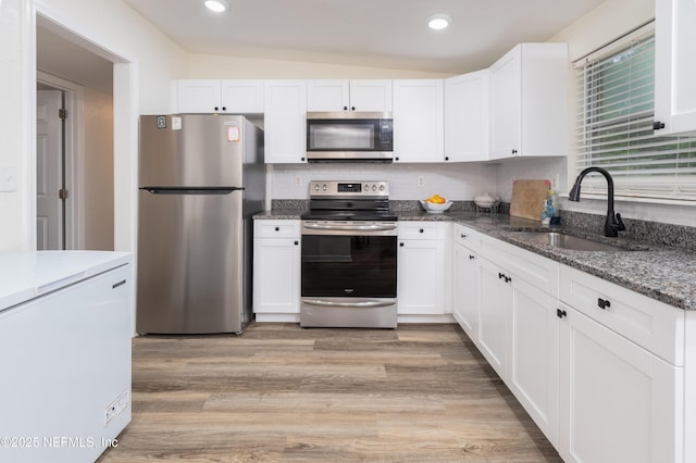3165 Victoria Park Rd, Jacksonville, FL 32216 - kitchen featuring lofted ceiling, dark stone counters, white cabinets, a sink, and appliances with stainless steel finishes