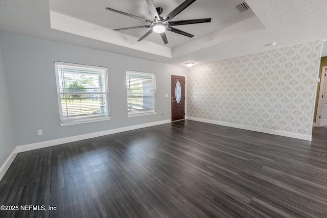 unfurnished living room featuring visible vents, a raised ceiling, ceiling fan, and baseboards