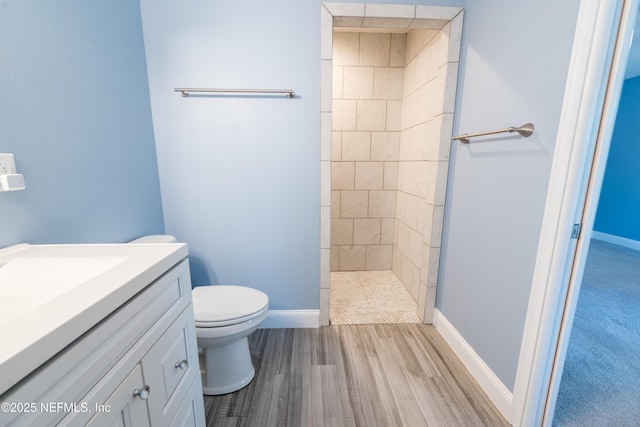 bathroom with baseboards, vanity, toilet, and tiled shower