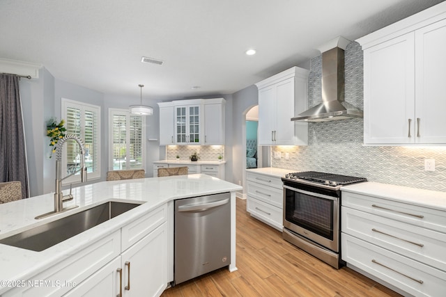 14526 Starbuck Springs Way, Jacksonville, FL 32258 - kitchen featuring wall chimney range hood, stainless steel appliances, arched walkways, white cabinetry, and decorative backsplash