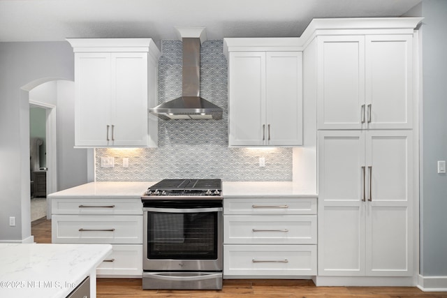 14526 Starbuck Springs Way, Jacksonville, FL 32258 - kitchen featuring stainless steel range oven, wall chimney exhaust hood, white cabinetry, tasteful backsplash, and arched walkways