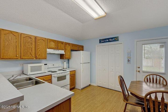 kitchen featuring a sink, light countertops, light wood finished floors, under cabinet range hood, and white appliances