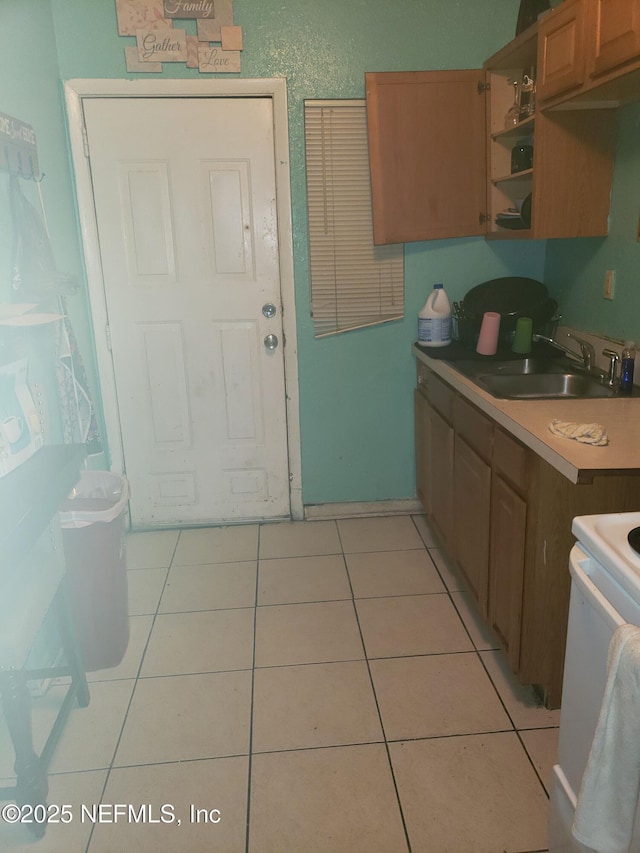 kitchen with open shelves, light tile patterned flooring, light countertops, a sink, and range