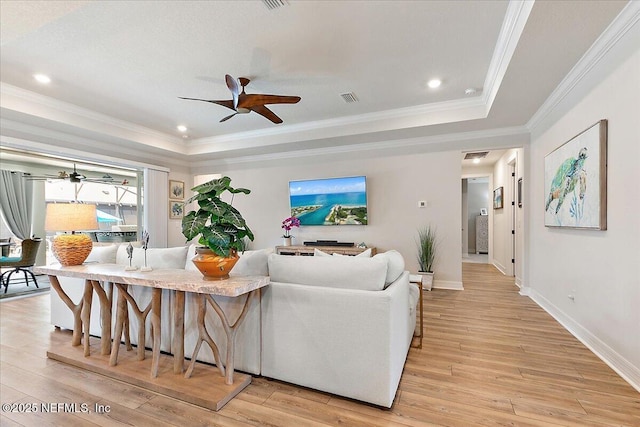 living area with visible vents, a ceiling fan, a raised ceiling, and light wood finished floors