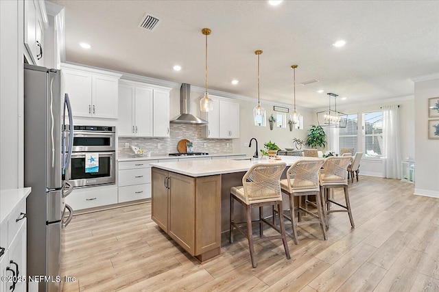 kitchen featuring wall chimney range hood, a sink, ornamental molding, stainless steel appliances, and light wood-style flooring