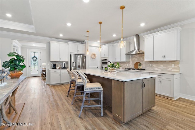 kitchen featuring an island with sink, wall chimney exhaust hood, white cabinetry, gas stovetop, and ornamental molding