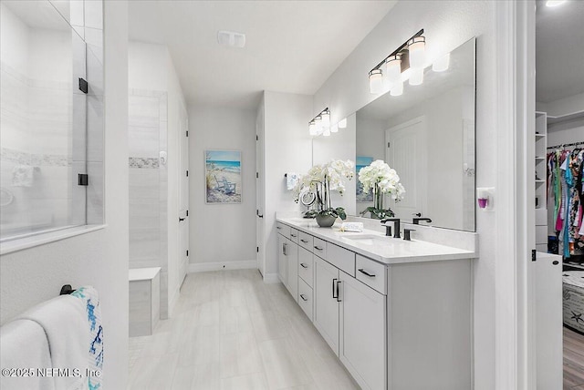 bathroom featuring vanity, baseboards, a tile shower, and a spacious closet