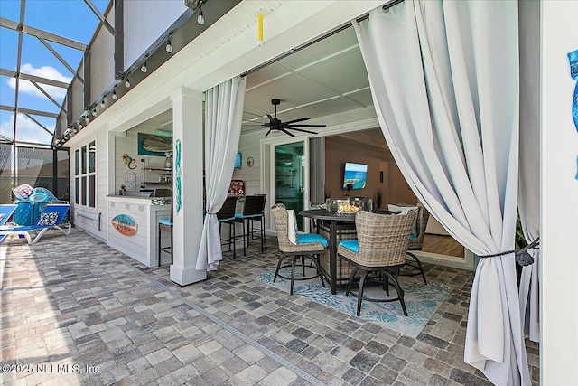 view of patio / terrace featuring a ceiling fan, outdoor dining space, and glass enclosure
