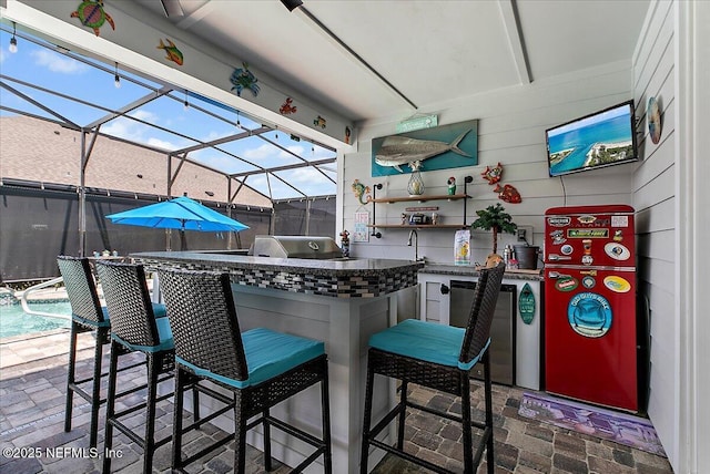 view of patio featuring a lanai, a swimming pool, outdoor wet bar, and an outdoor kitchen