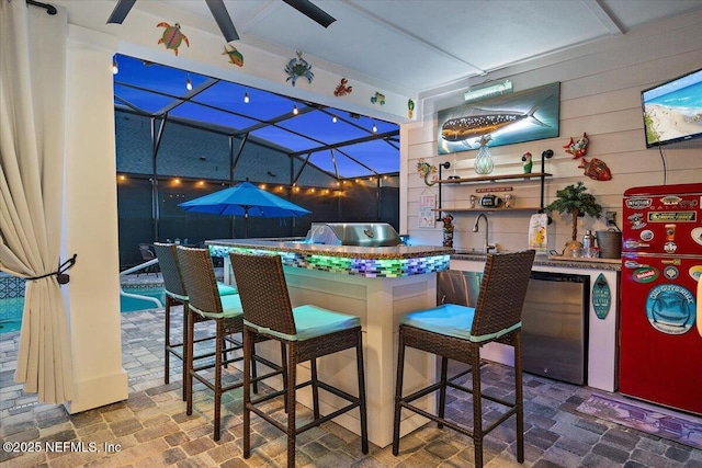 view of patio / terrace featuring area for grilling, ceiling fan, glass enclosure, a sink, and outdoor wet bar