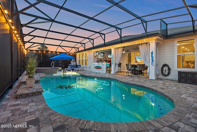 pool featuring a ceiling fan, glass enclosure, a patio area, and an outdoor kitchen