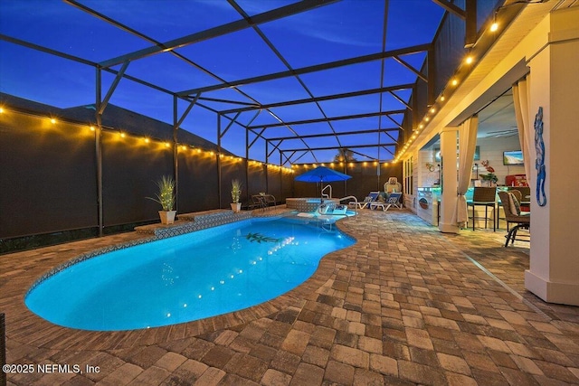 pool at night with a lanai, a pool with connected hot tub, and a patio area