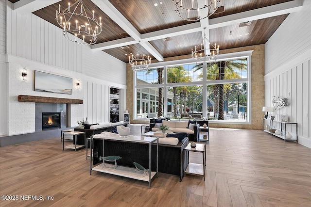 living room with a glass covered fireplace, a high ceiling, a chandelier, and beamed ceiling