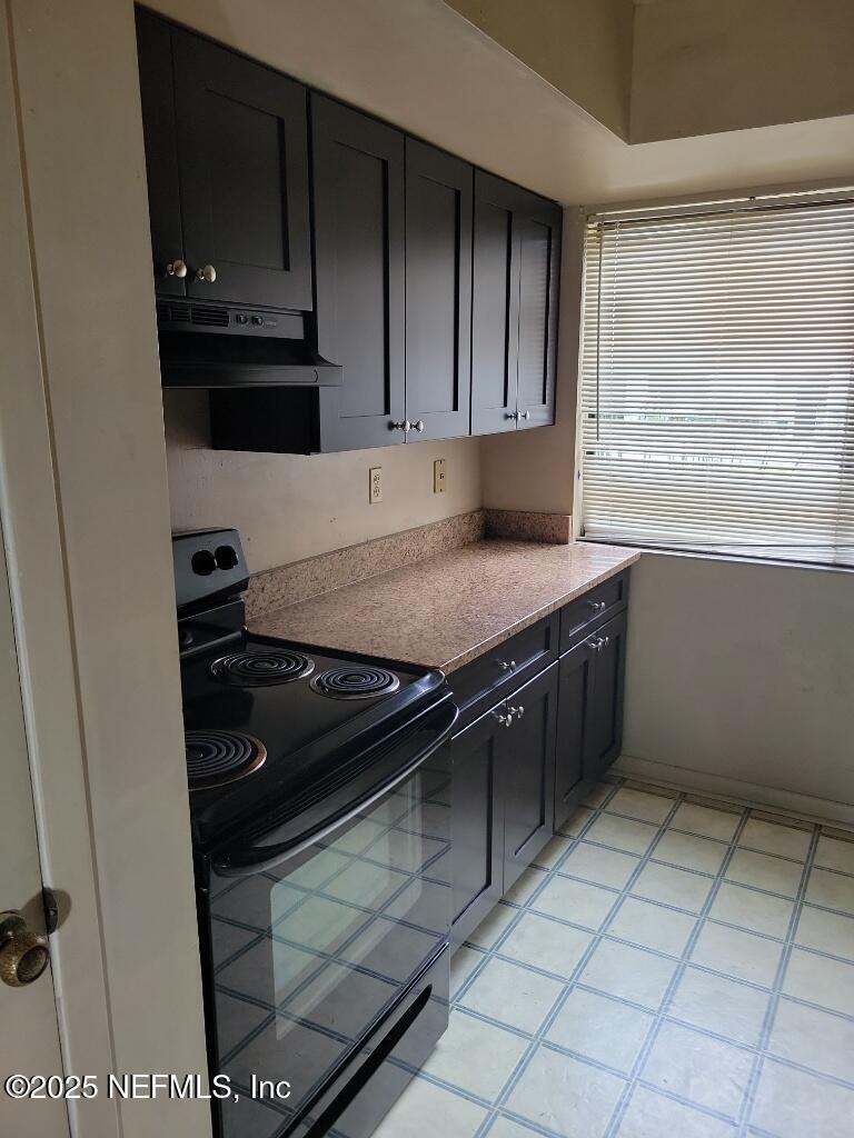 kitchen with dark cabinets, black / electric stove, light tile patterned flooring, and under cabinet range hood