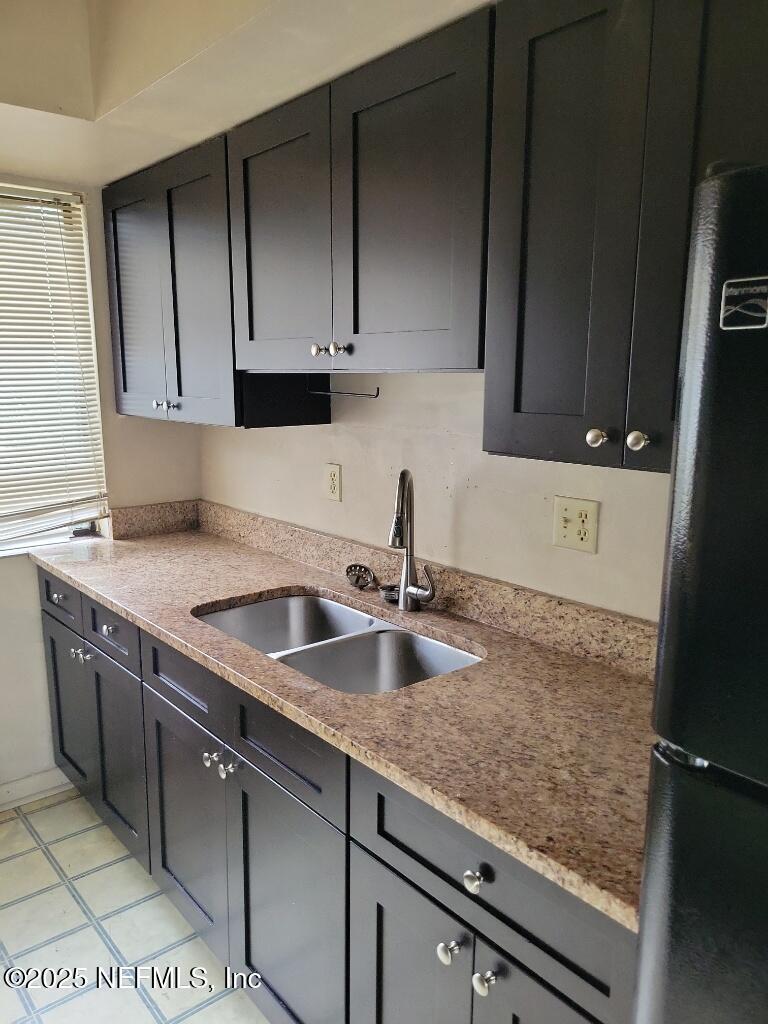 kitchen with freestanding refrigerator, light stone counters, light tile patterned flooring, and a sink