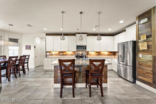 341 Aspen Leaf Dr, Jacksonville, FL 32081 - kitchen featuring appliances with stainless steel finishes, decorative backsplash, a textured ceiling, pendant lighting, and a center island with sink