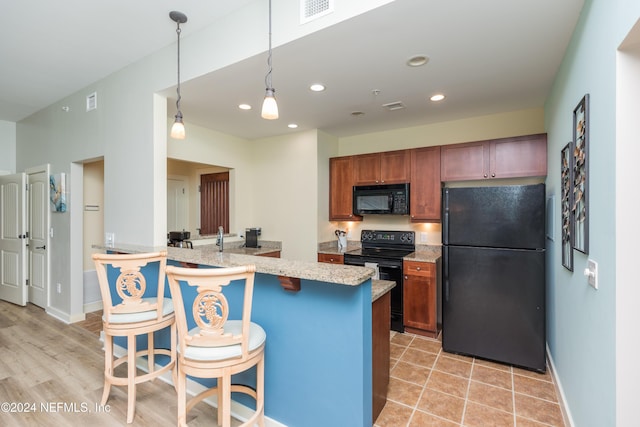 kitchen with brown cabinets, a breakfast bar, light stone counters, black appliances, and visible vents