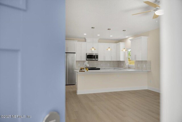 kitchen featuring light countertops, a sink, light wood finished floors, appliances with stainless steel finishes, and backsplash