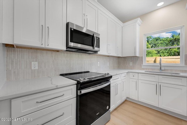 kitchen with electric range, stainless steel microwave, white cabinets, light stone counters, and a sink