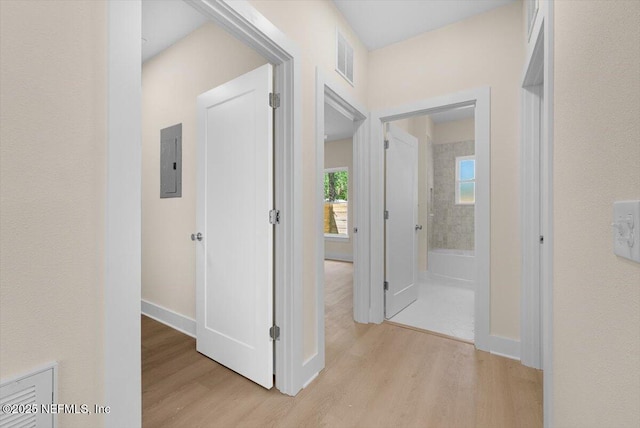 hall featuring baseboards, light wood-style floors, visible vents, and electric panel