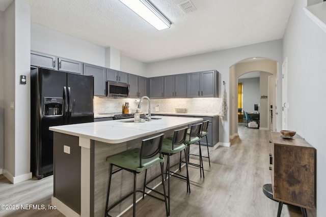 625 Oakleaf Plantation Pkwy Unit 1115, Orange Park, FL 32065 - kitchen featuring stainless steel microwave, tasteful backsplash, black fridge, arched walkways, and light wood-style floors