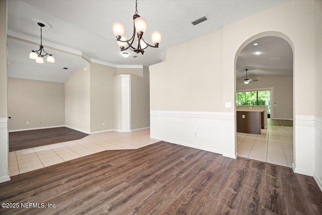 unfurnished room with lofted ceiling, ceiling fan with notable chandelier, wood finished floors, visible vents, and arched walkways