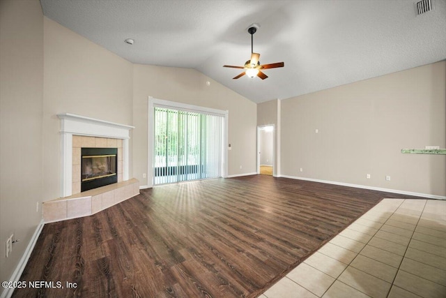 unfurnished living room with a tile fireplace, wood finished floors, a ceiling fan, visible vents, and lofted ceiling
