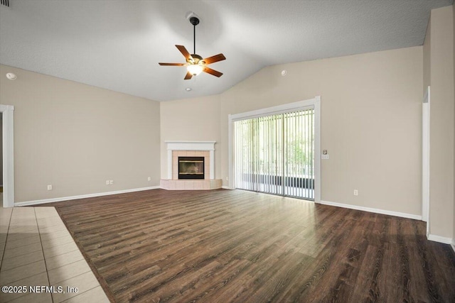 unfurnished living room with wood finished floors, a tiled fireplace, baseboards, ceiling fan, and vaulted ceiling
