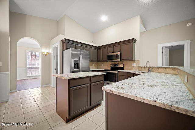 kitchen with dark brown cabinets, light stone counters, a sink, decorative backsplash, and stainless steel appliances