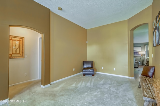 unfurnished room featuring a textured ceiling, carpet flooring, arched walkways, and baseboards
