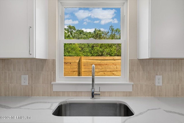 interior details featuring a sink, white cabinets, light stone countertops, and tasteful backsplash