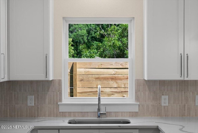 kitchen with a sink, white cabinetry, backsplash, and a wealth of natural light