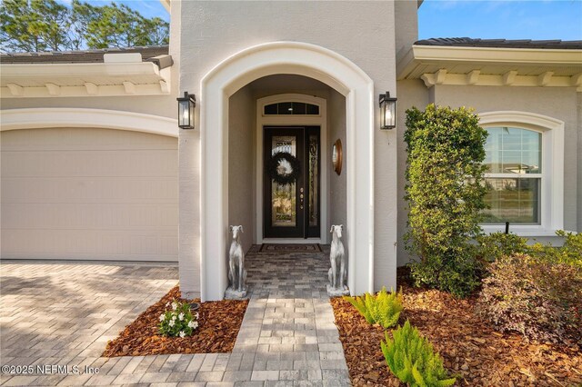 view of exterior entry with stucco siding, a garage, and driveway