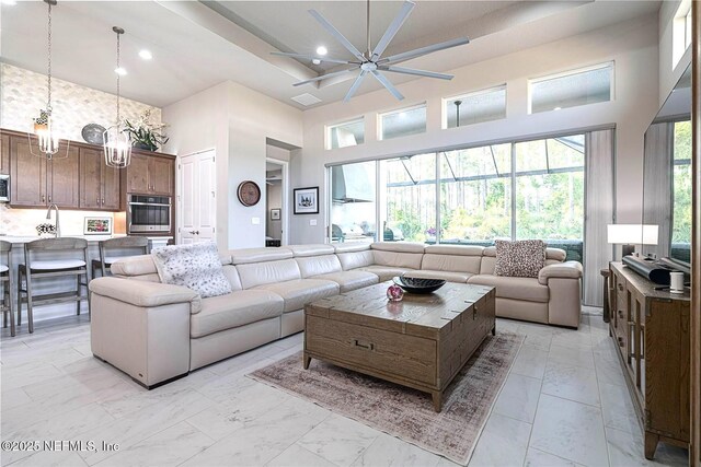 living room featuring a towering ceiling, ceiling fan, light marble finish floors, recessed lighting, and a chandelier