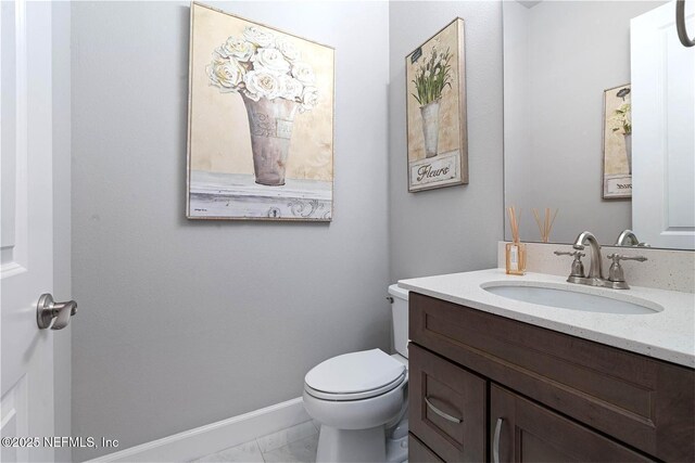 half bath with marble look tile flooring, vanity, toilet, and baseboards